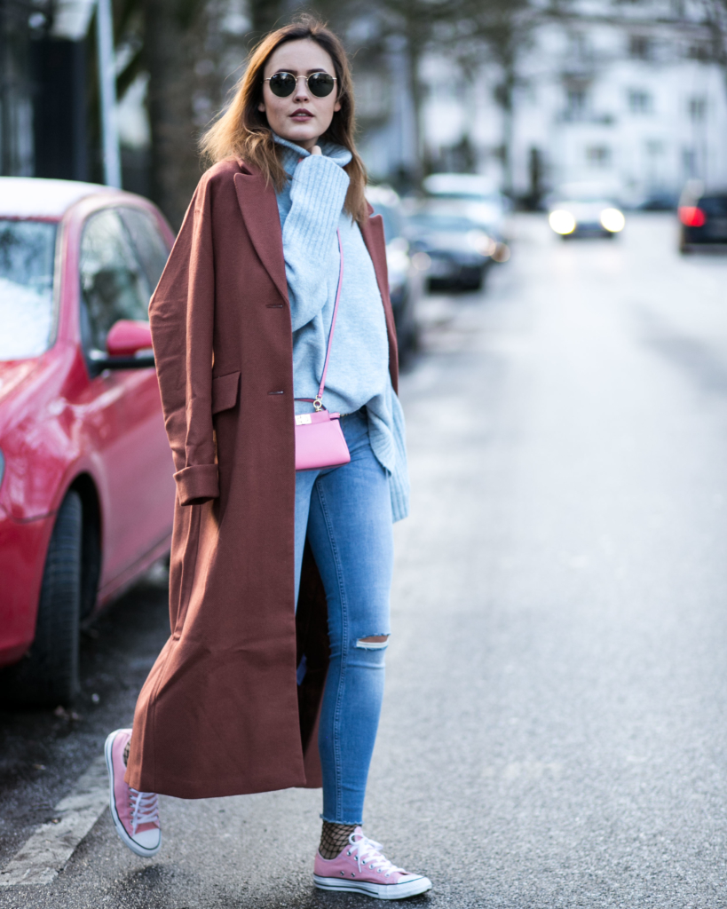  rosa farbigen Accessoires auf: Pinke Chucks und eine mini kleine pinke Crossbody Tasche, Skinny Jeans, gestrickten hellblauen Rollkragenpullover, extra langen Mantel von Edited the Label in Cogna