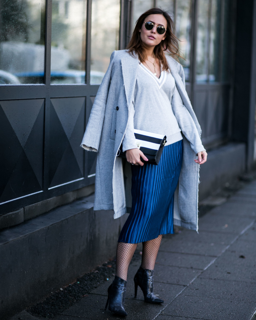hohe schwarze spitze Stiefeletten in Schlangenleder Optik, mittellangen blauen Plissee Rock, lässiges Sweatshirt mit tiefem V-Ausschnitt, langer Wollmantel in hellblau