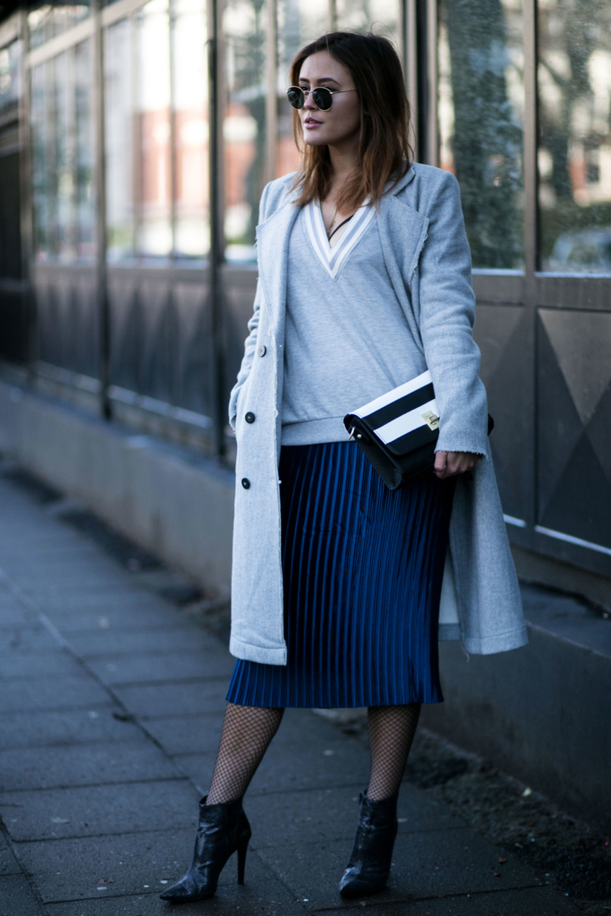 Sonnenbrille, lässiges Sweatshirt mit tiefem V-Ausschnitt, langer Wollmantel in hellblauhohe schwarze spitze Stiefeletten in Schlangenleder Optik, mittellangen blauen Plissee Rock