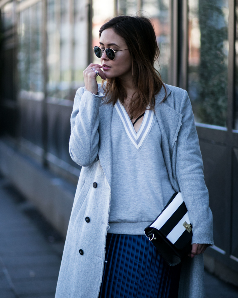 lässiges Sweatshirt mit tiefem V-Ausschnitt, langer Wollmantel in hellblauhohe schwarze spitze Stiefeletten in Schlangenleder Optik, mittellangen blauen Plissee Rock