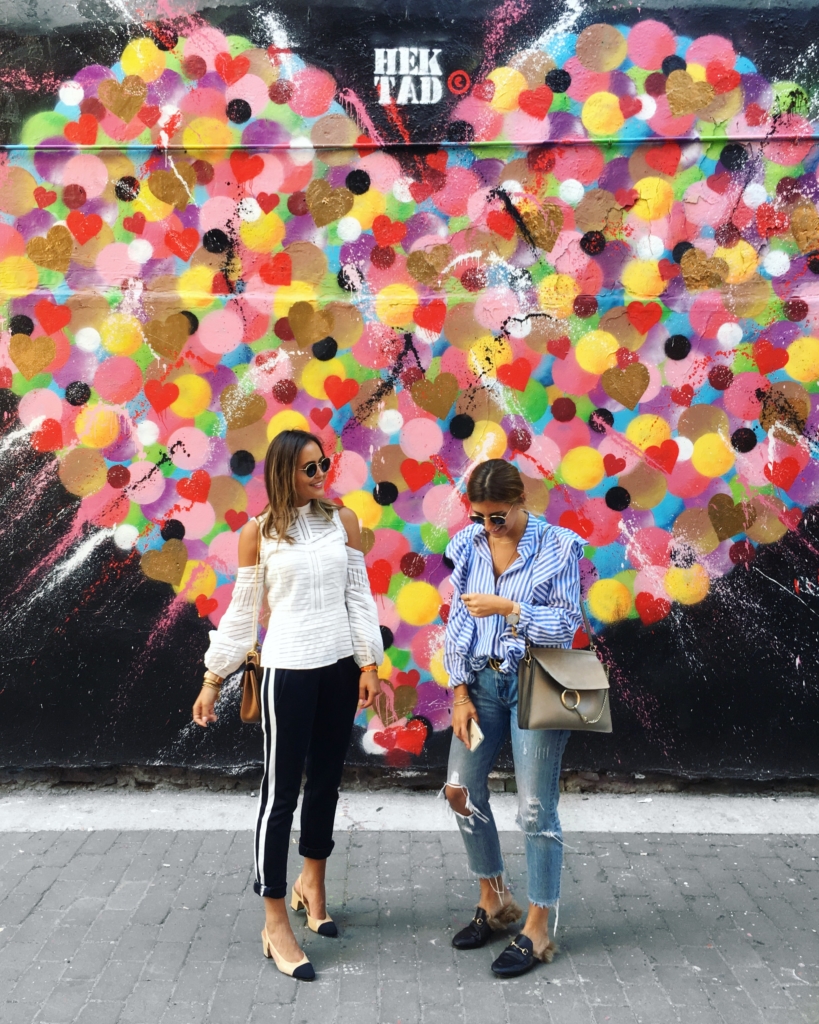 Bild vor Kunstwerk, Jogginhose, Pumps, Bluse, Sonnenbrille 